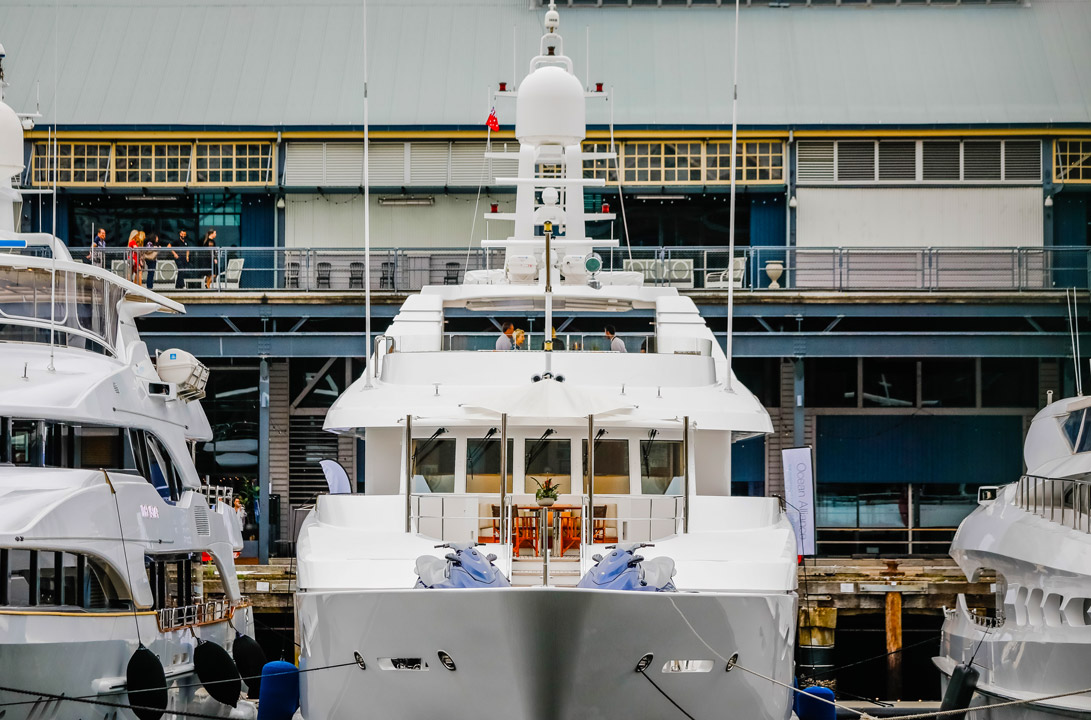 White superyacht docked with Jones Bay Wharf in background, with blue jetskis on deck.